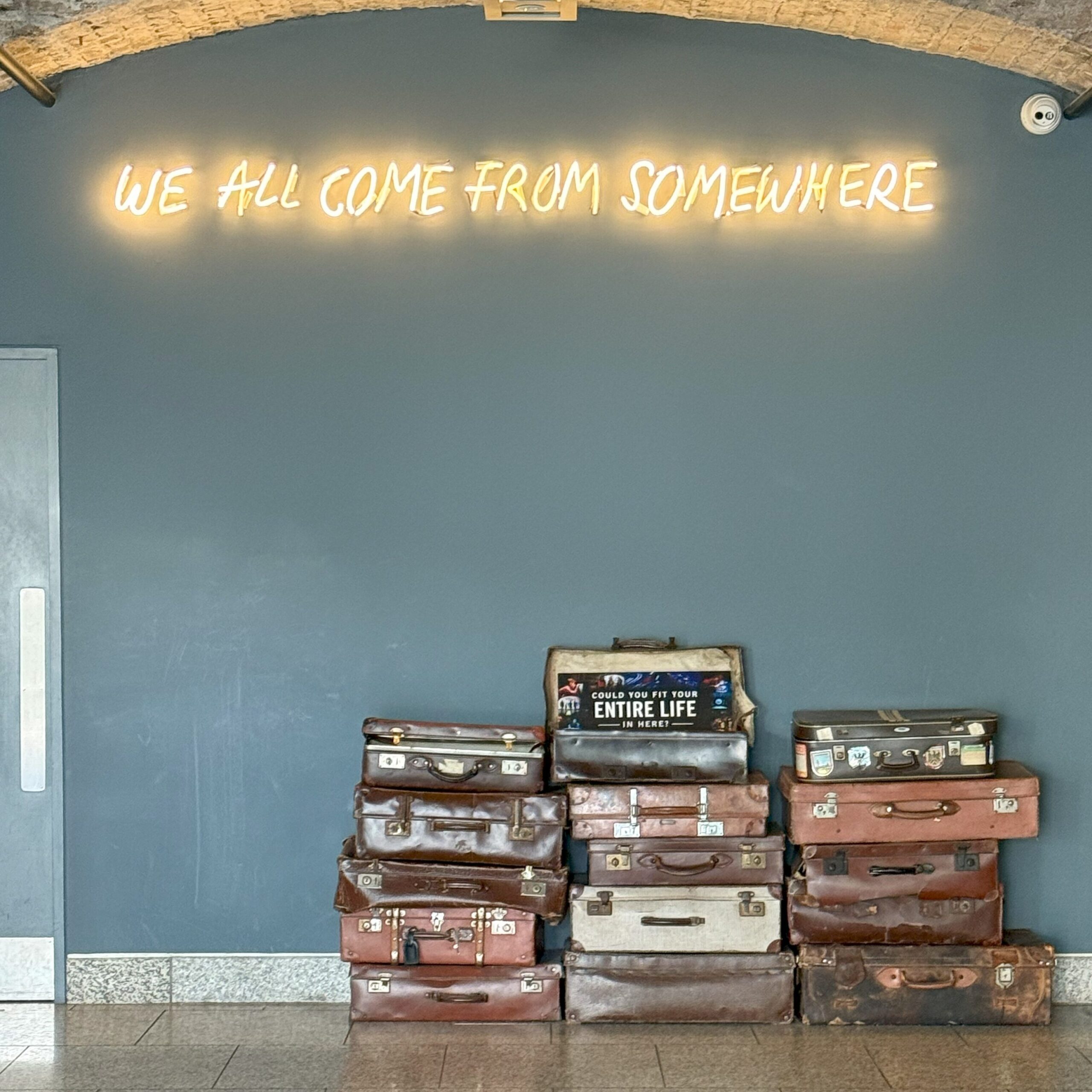 We All Come From Somewhere sign in the EPIC museum in Dublin with vintage suitcases.